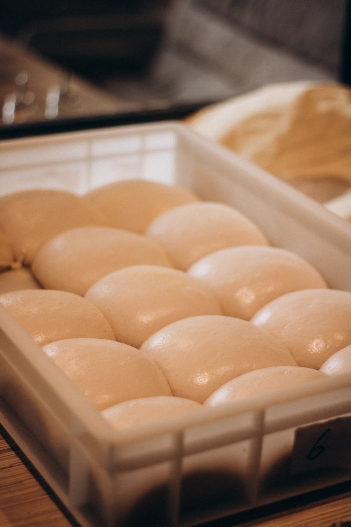 Close-up of smooth dough balls in a plastic tray, ideal for bread making or pizza preparation.