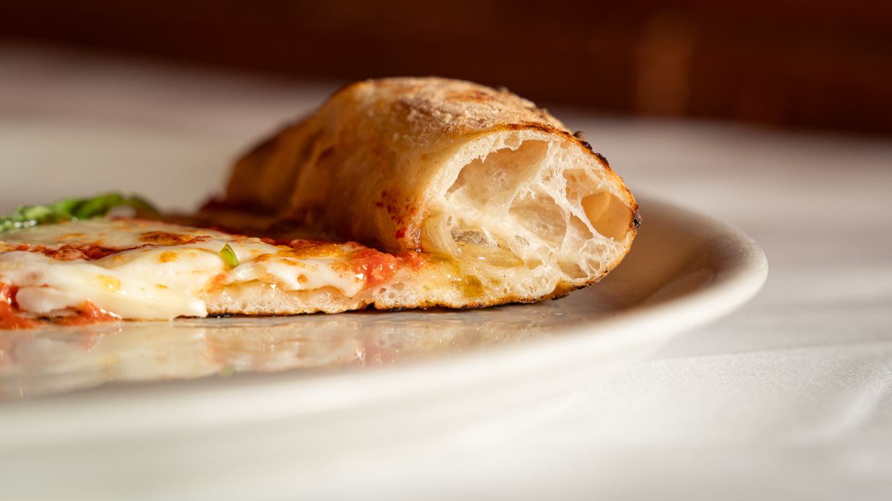 A detailed view of a fresh margarita pizza slice on a white plate, showing melted cheese and crust texture.